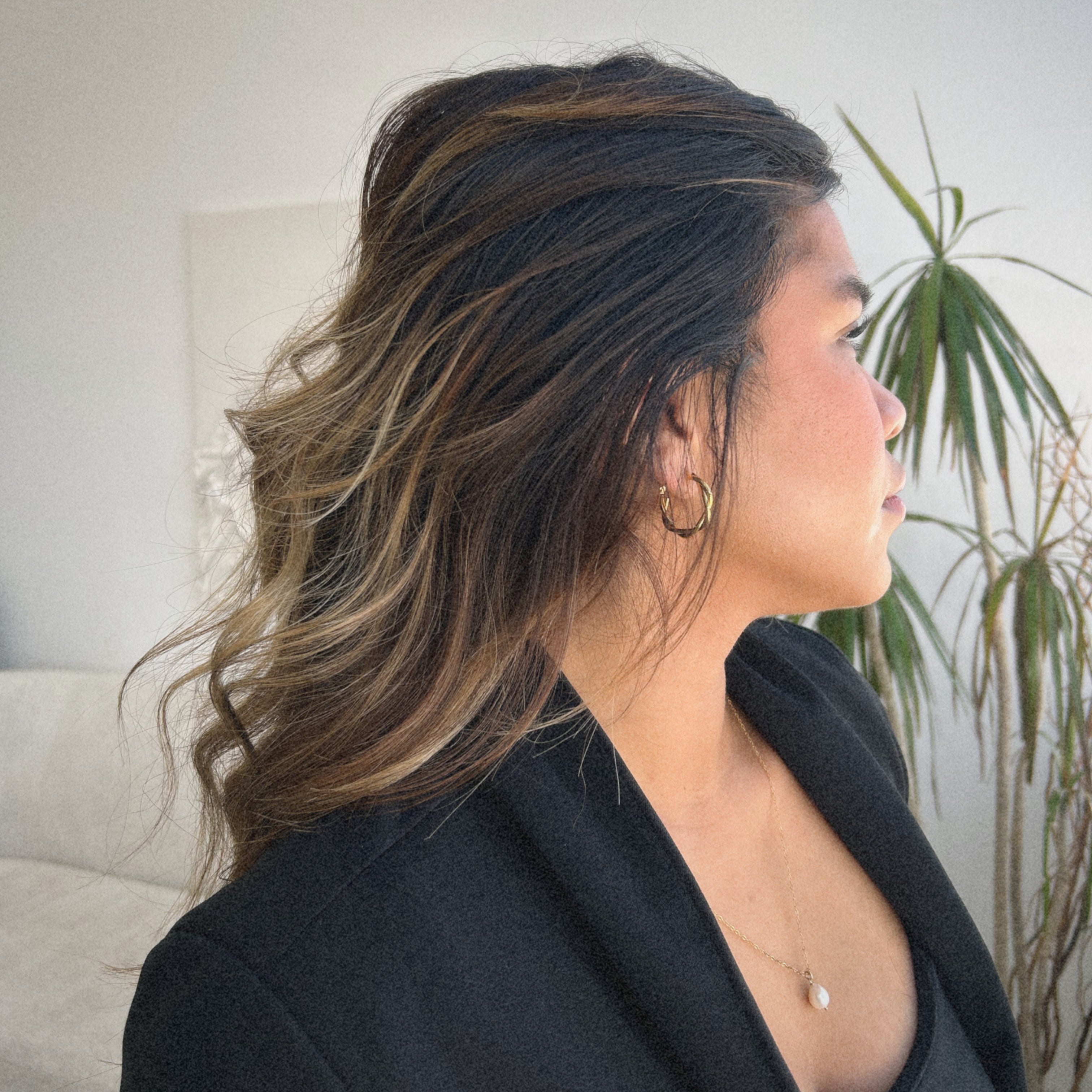 image of a woman looking off to the side wearing a gold twisted hoop and a pearl necklace
