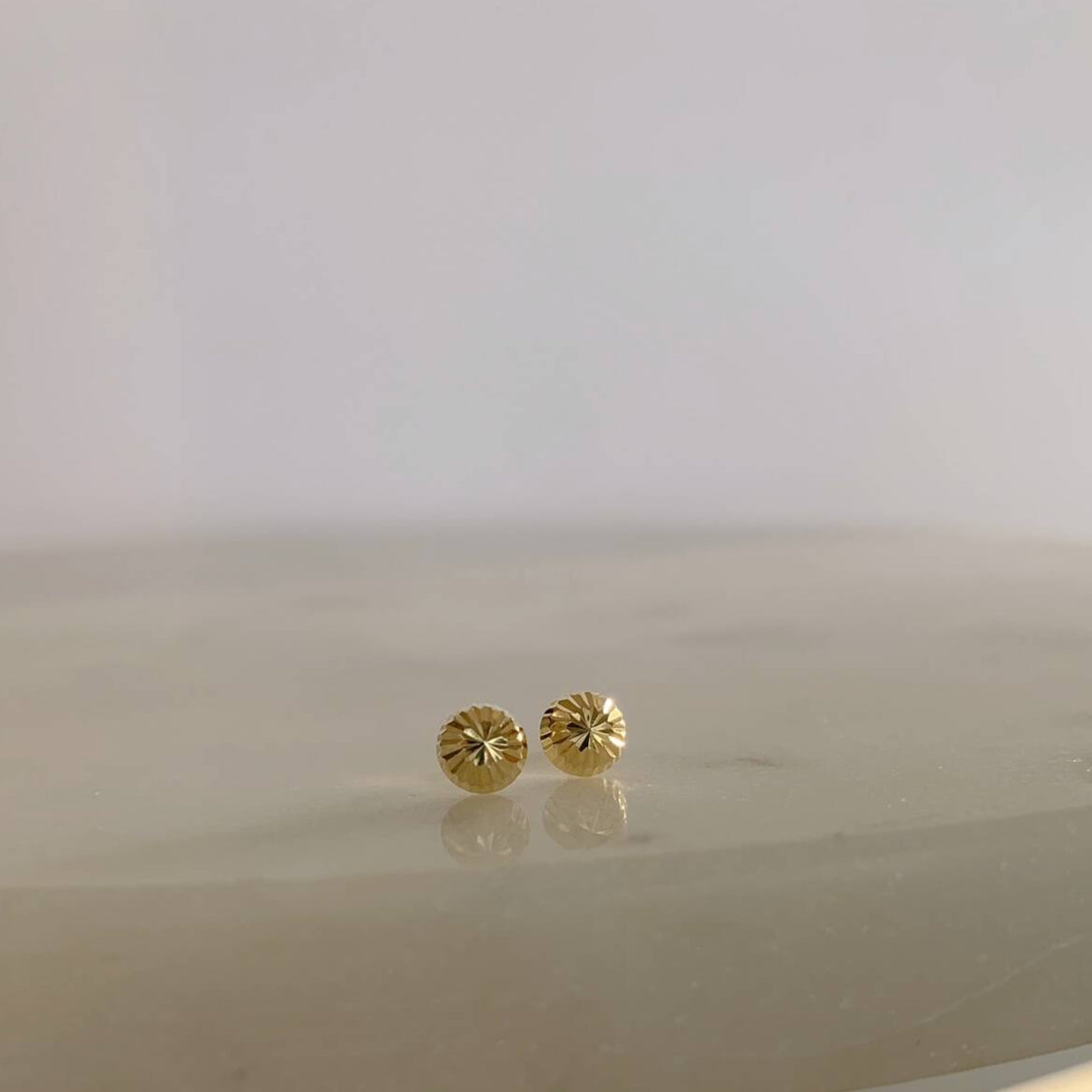 image of two diamond cut ball stud earrings on a marble table