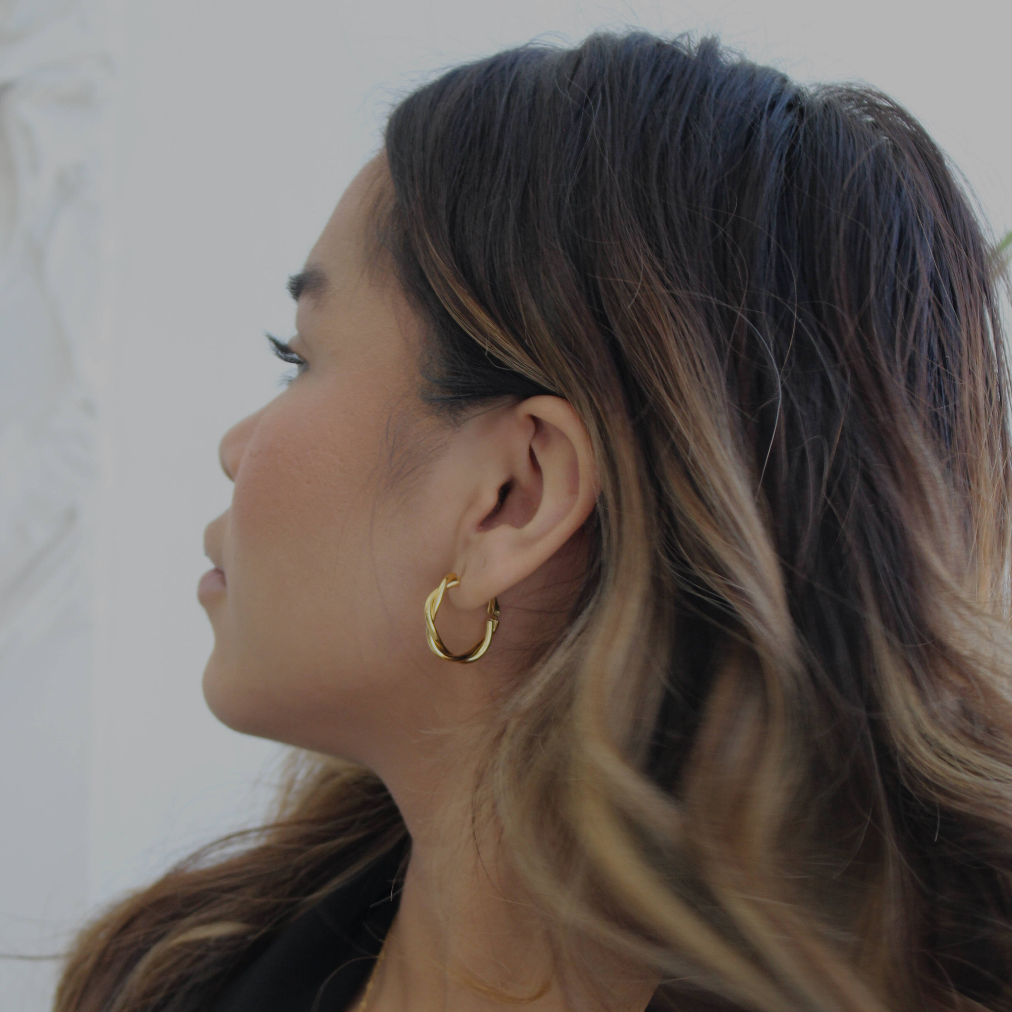 image of a woman wearing gold twisted hoops looking off to the side