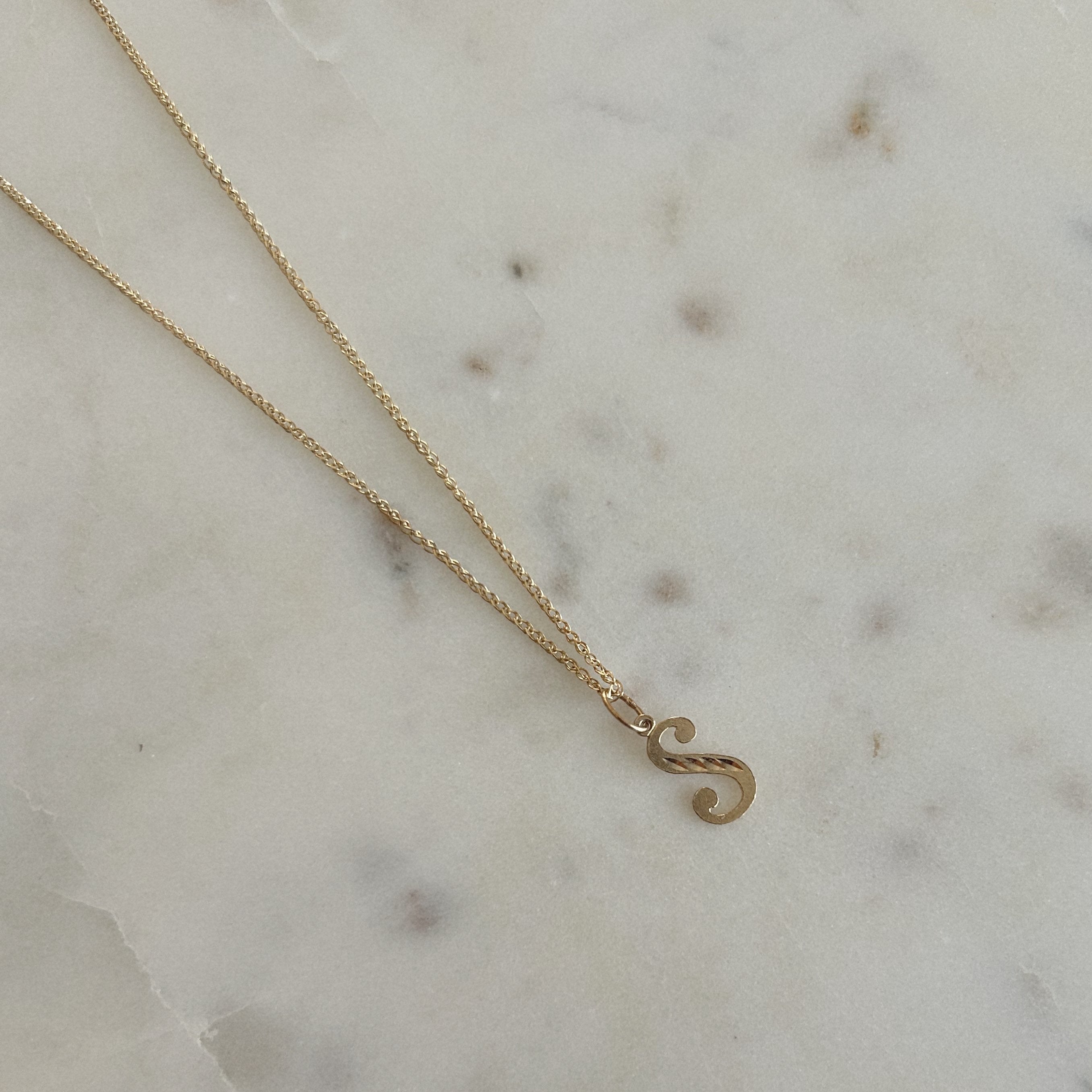 image of a 14k letter chain with the pendant letter s against a marble backdrop
