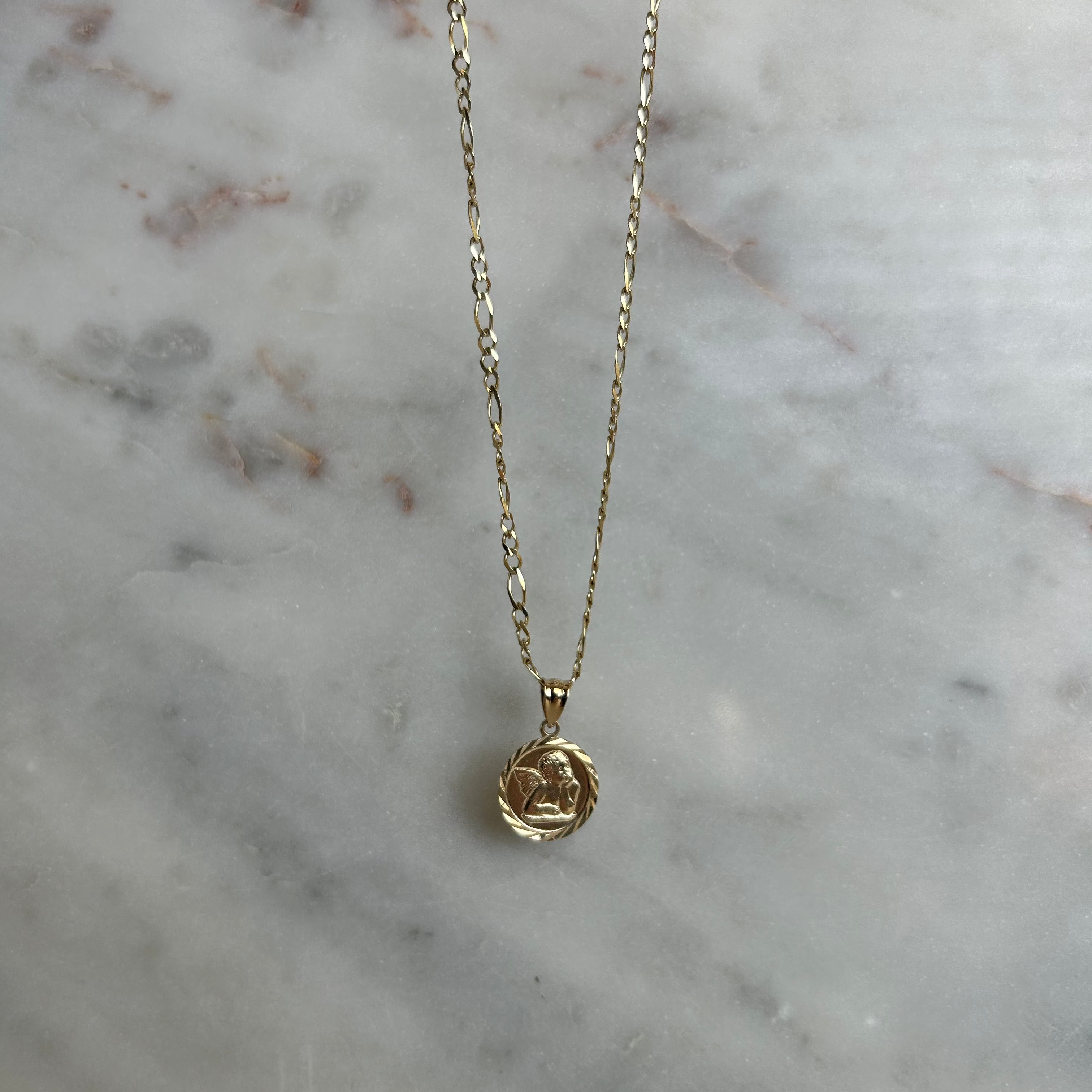 image of a gold angel pendant necklace on a marble backdrop