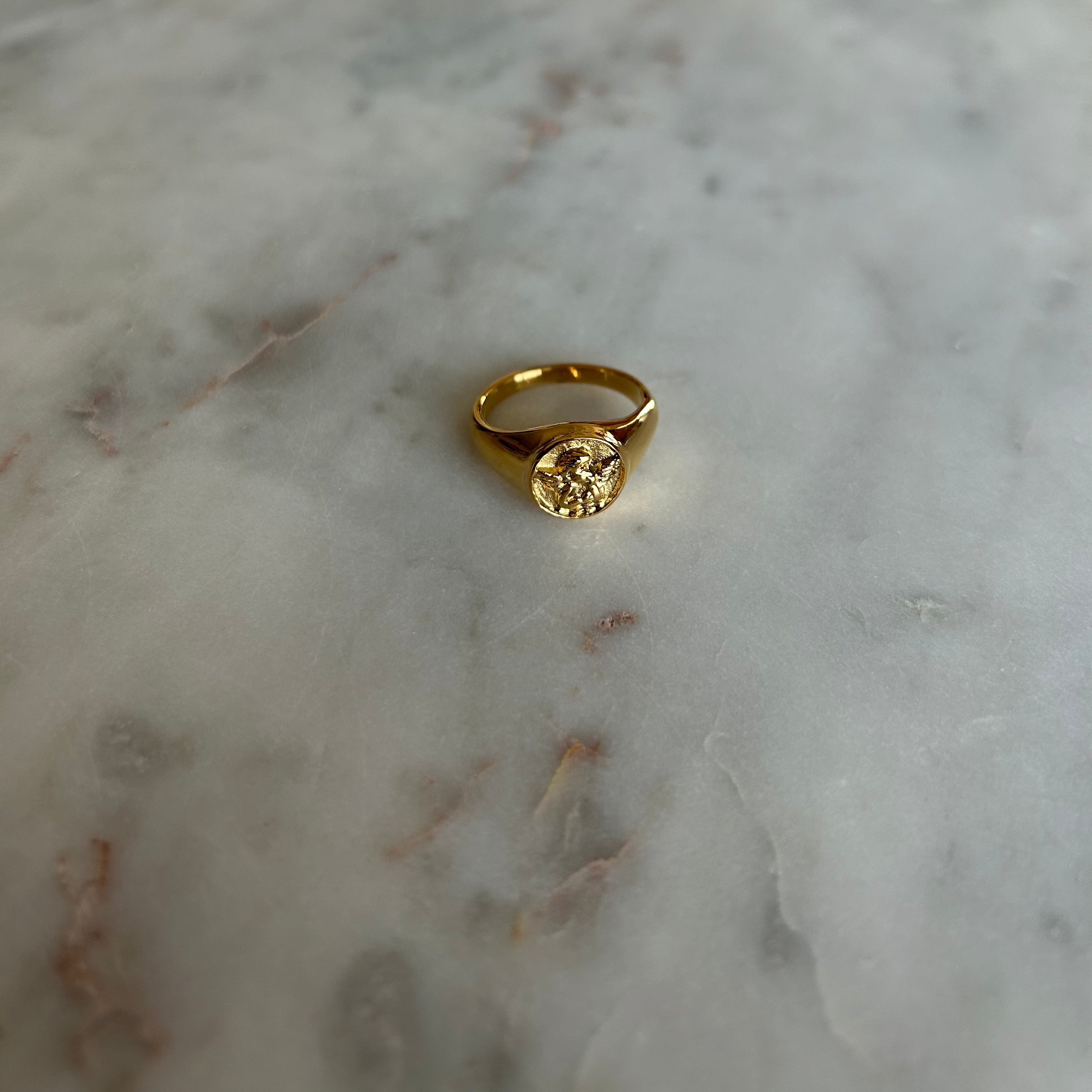 image of a gold angel signet ring on a marble table