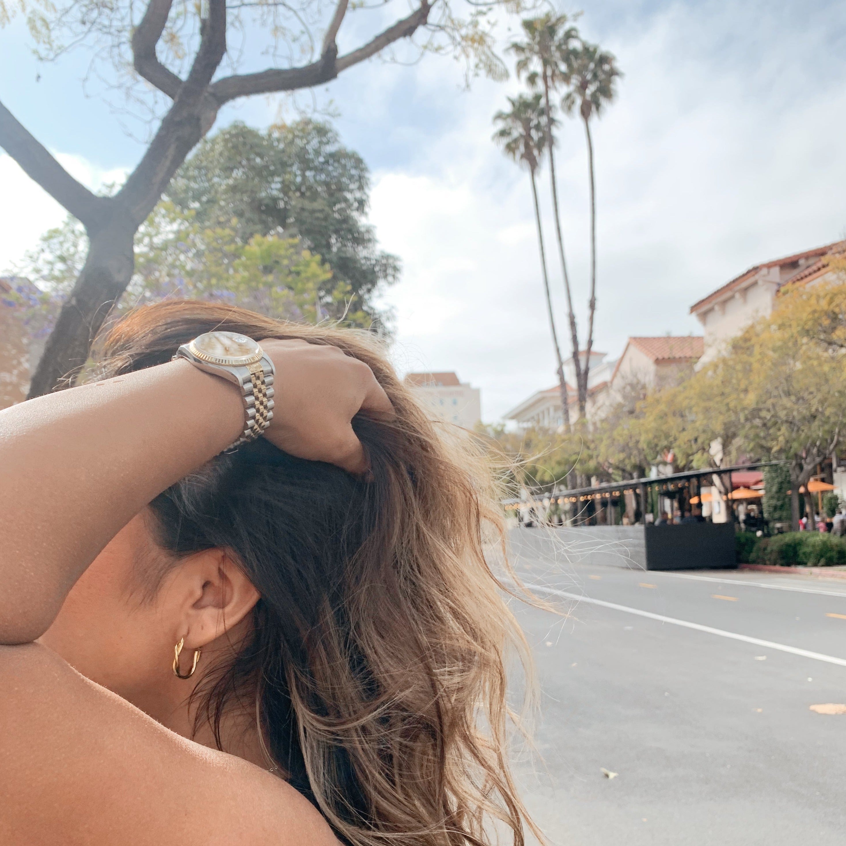 image of women holding her hair up wearing gold twisted hoops against a california backdrop with two palm trees