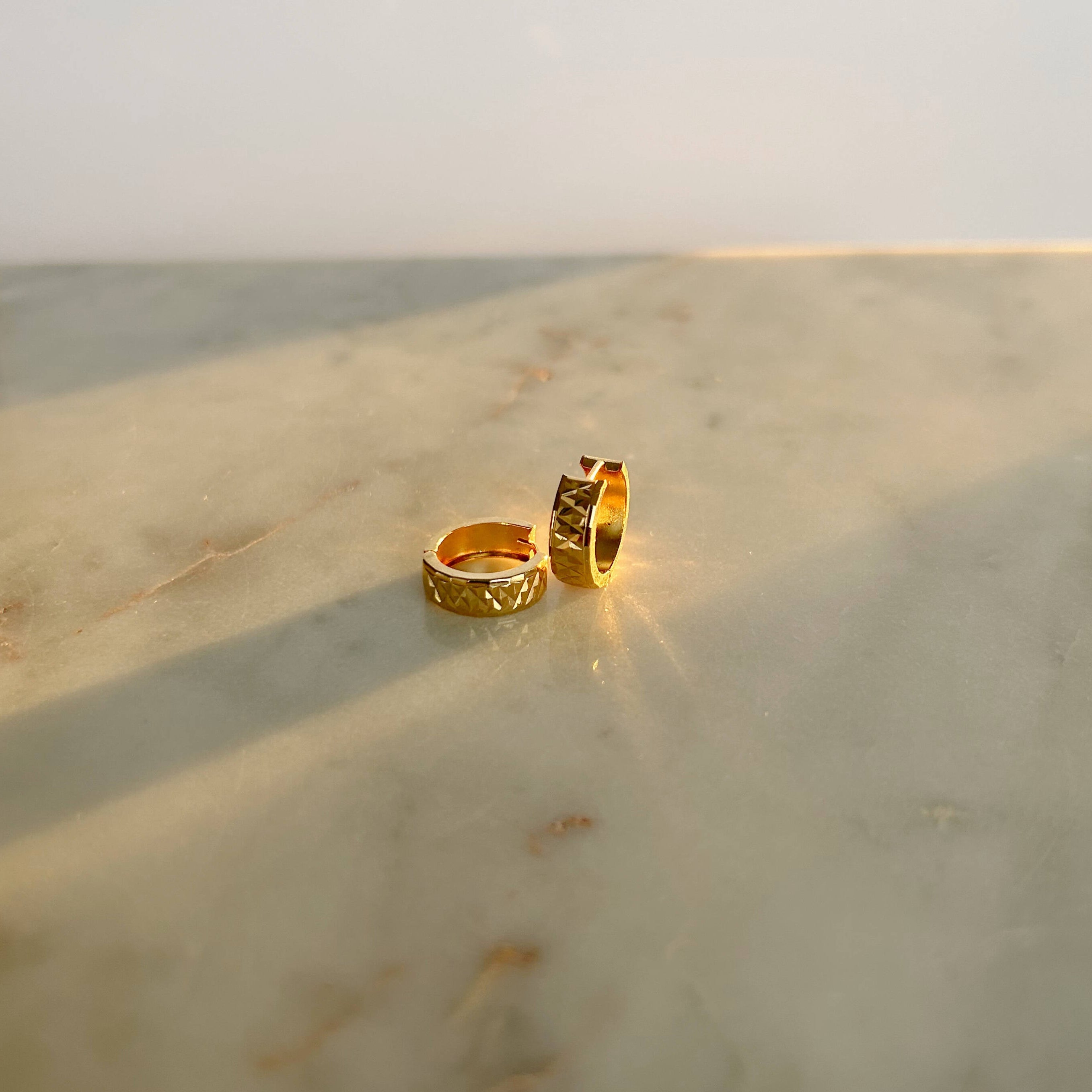 image of gold hoop earrings on a marble table against a white backdrop with the sunlight hitting in the back