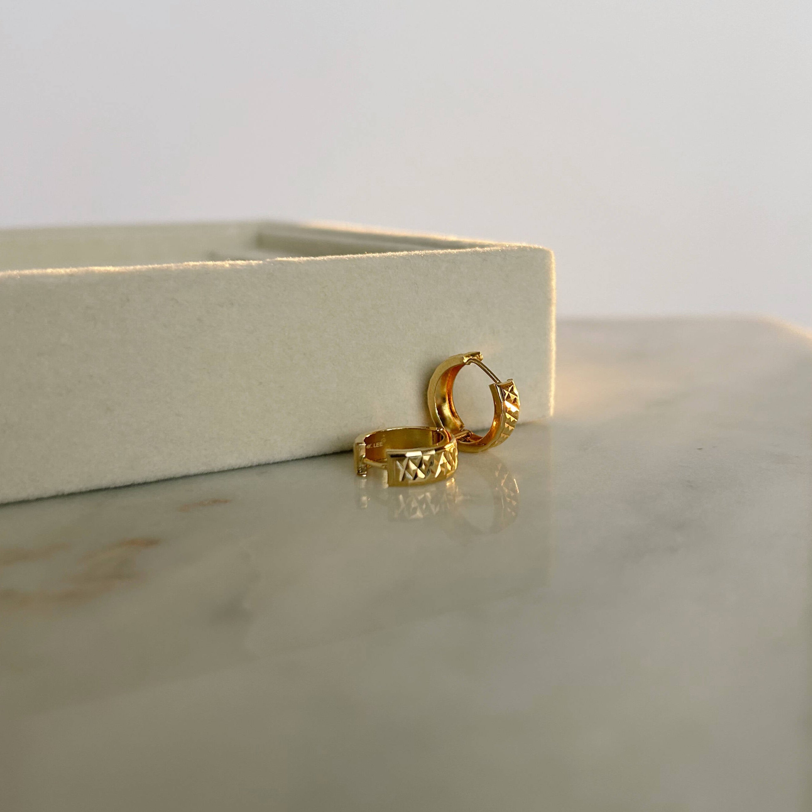 image of gold hoop earrings on a marble table against a jewelry ring holder and a white backdrop