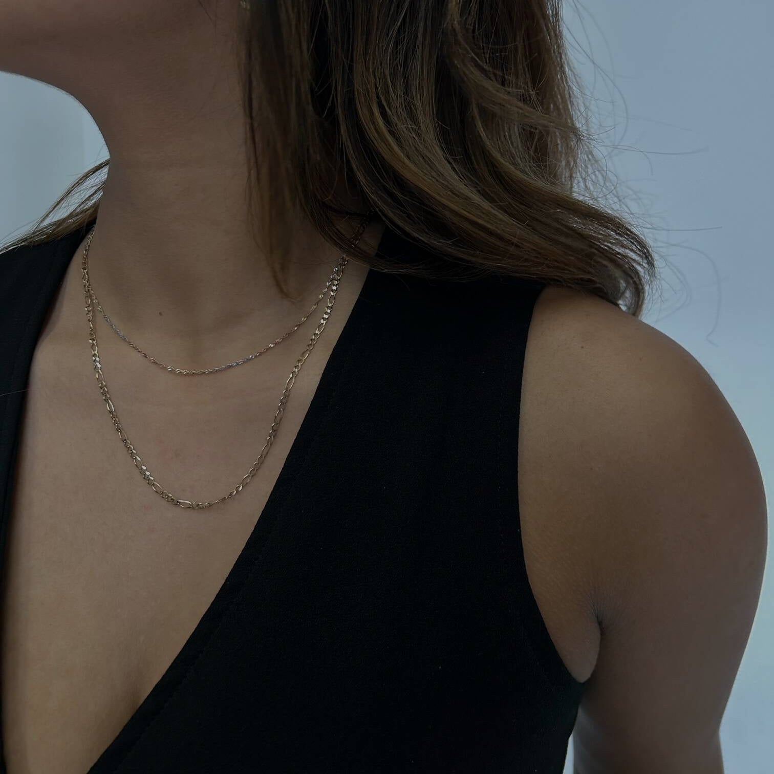 woman wearing a gold figaro chain against a white backdrop