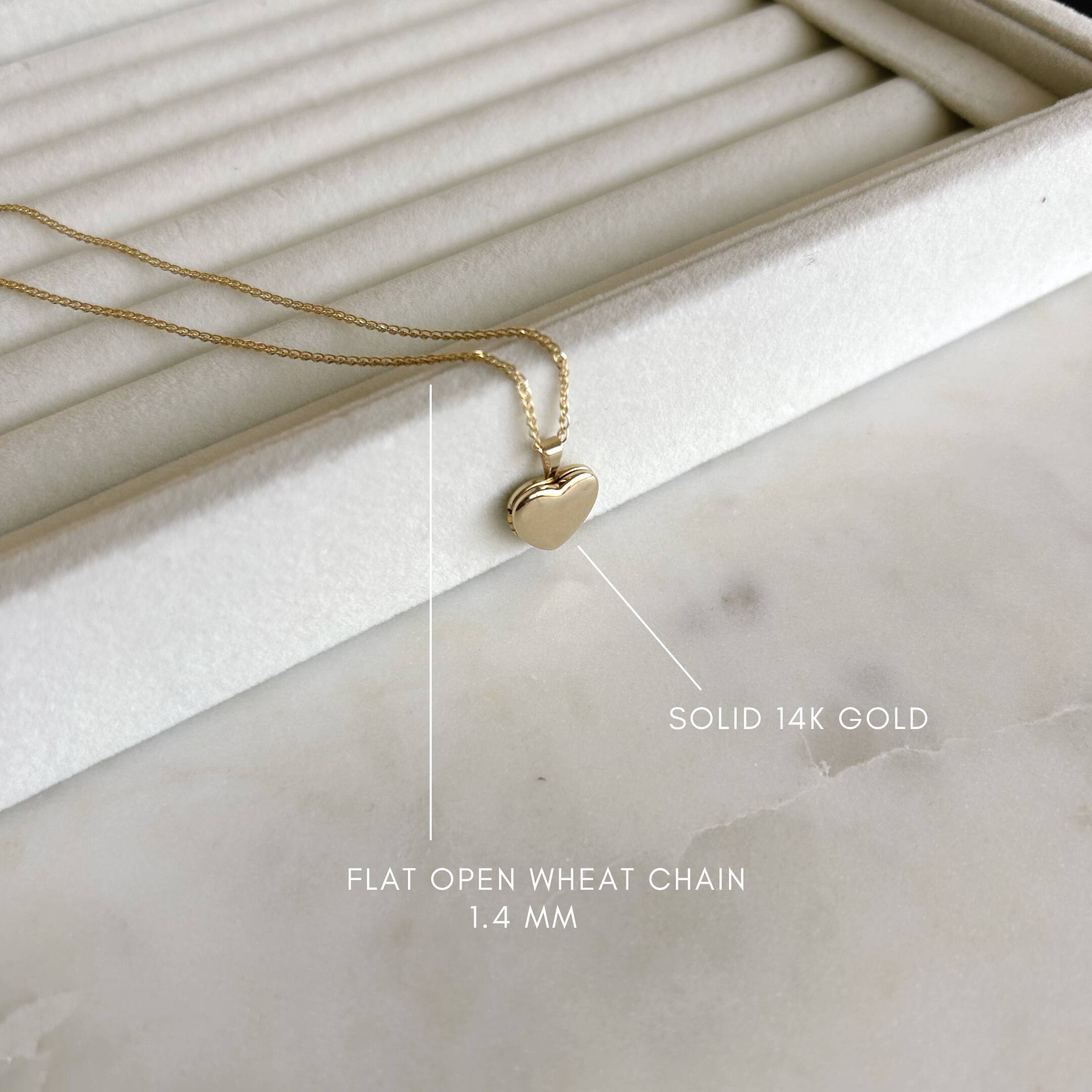 image of a gold heart locket on top of a jewelry ring tray with the descriptions of a solid 14k gold chain and the type of chain
