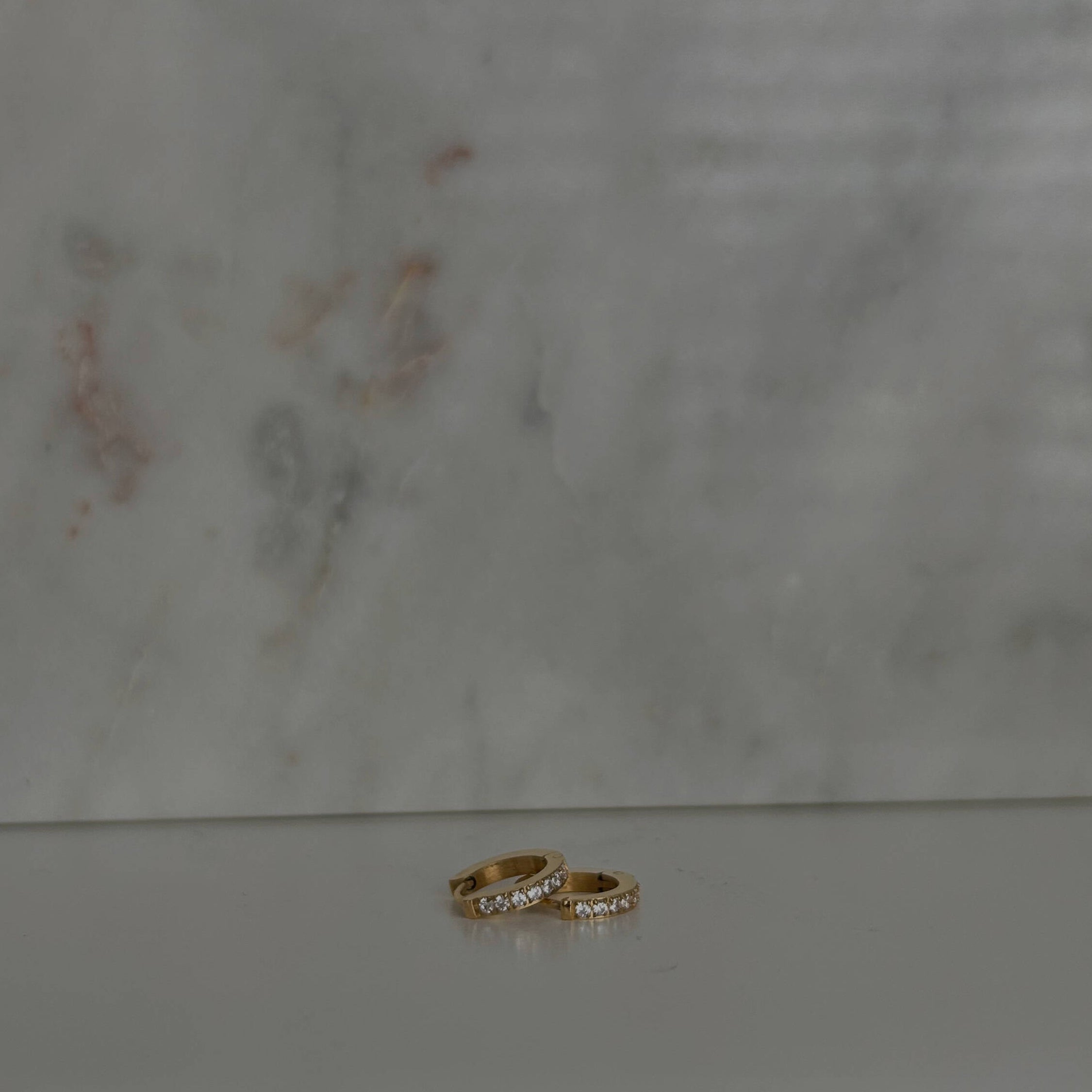 image of two gold earrings on top of each other against a marble backdrop