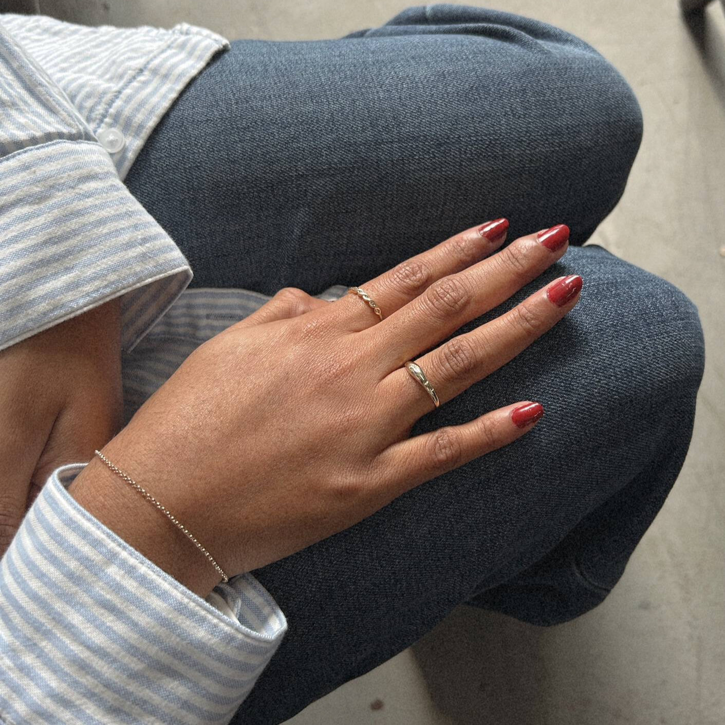image of a womans hands on her jeans with a gold bracelet and two gold rings