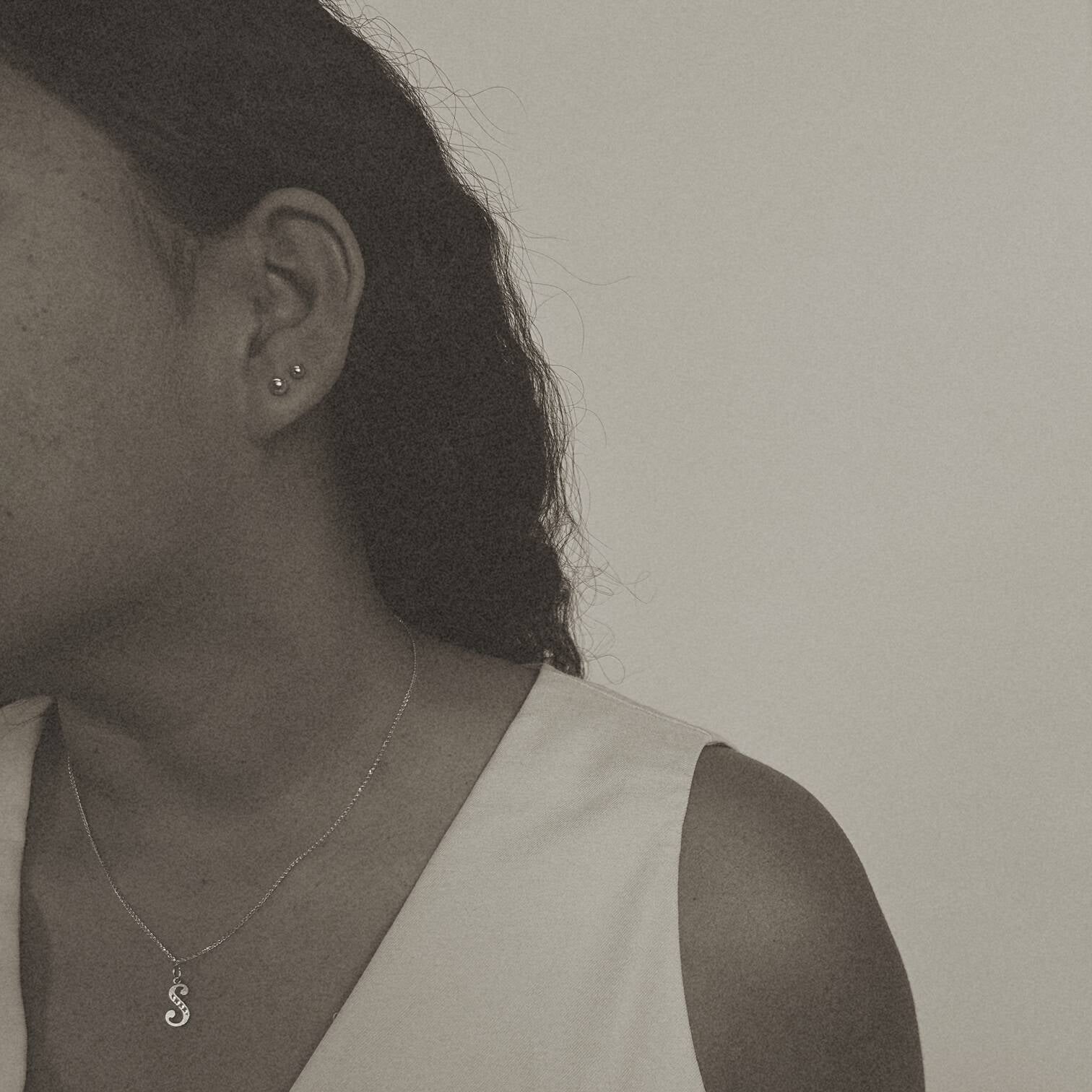 image of a woman wearing a gold s letter necklace and two gold ball stud earrings