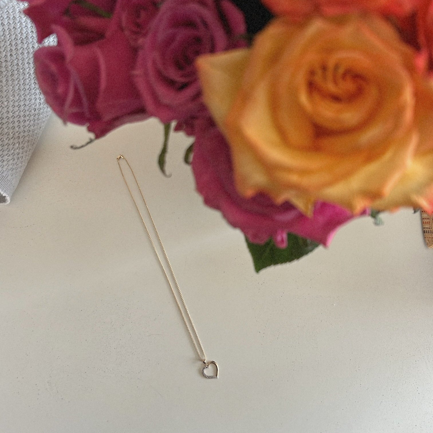 image of a heart necklace on a white table with a floral arrangement on the side