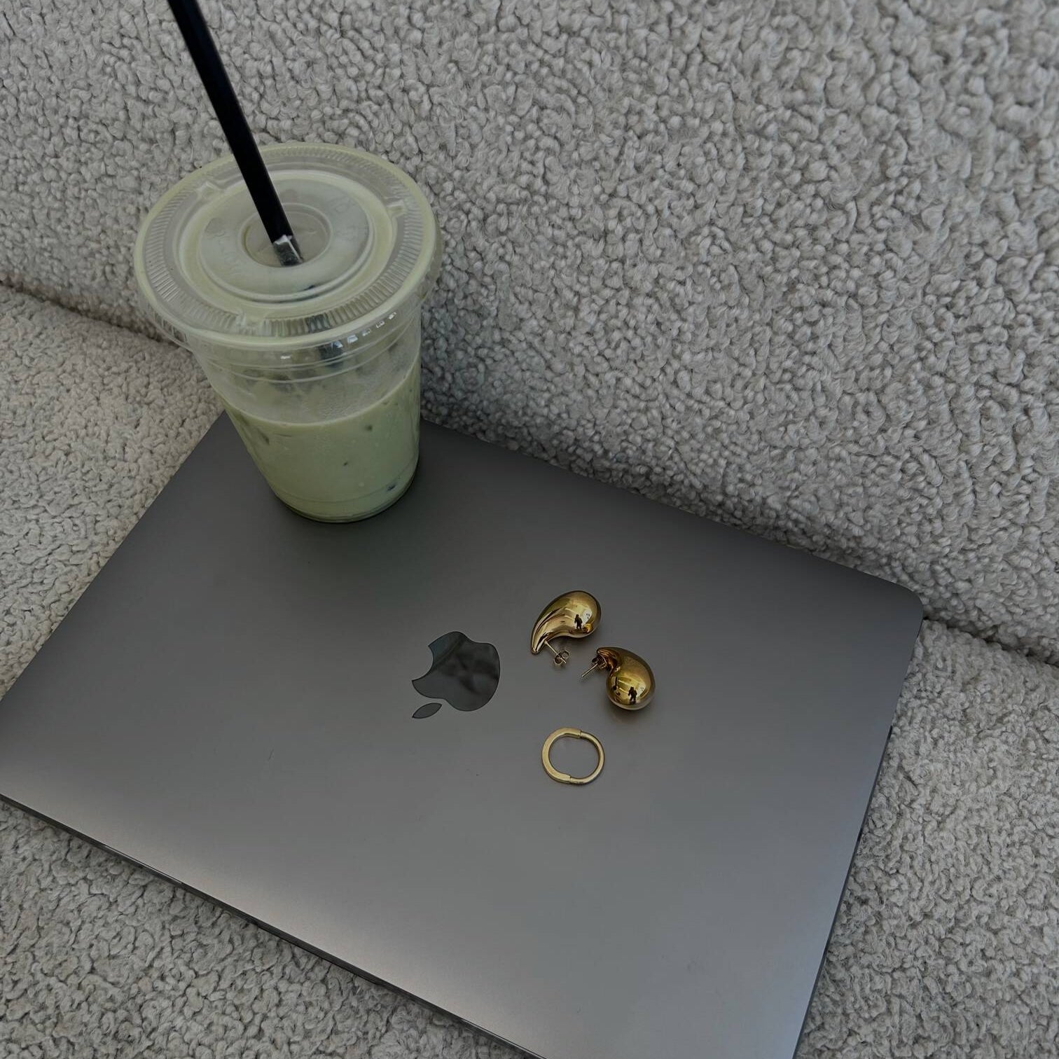picture of teardrop earrings on top of a macbook laptop on a couch with a match drink on the side