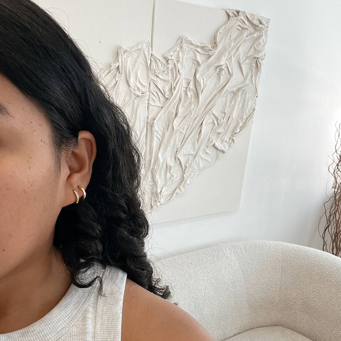 woman taking a selfie with two gold hoops on and a couch in the back