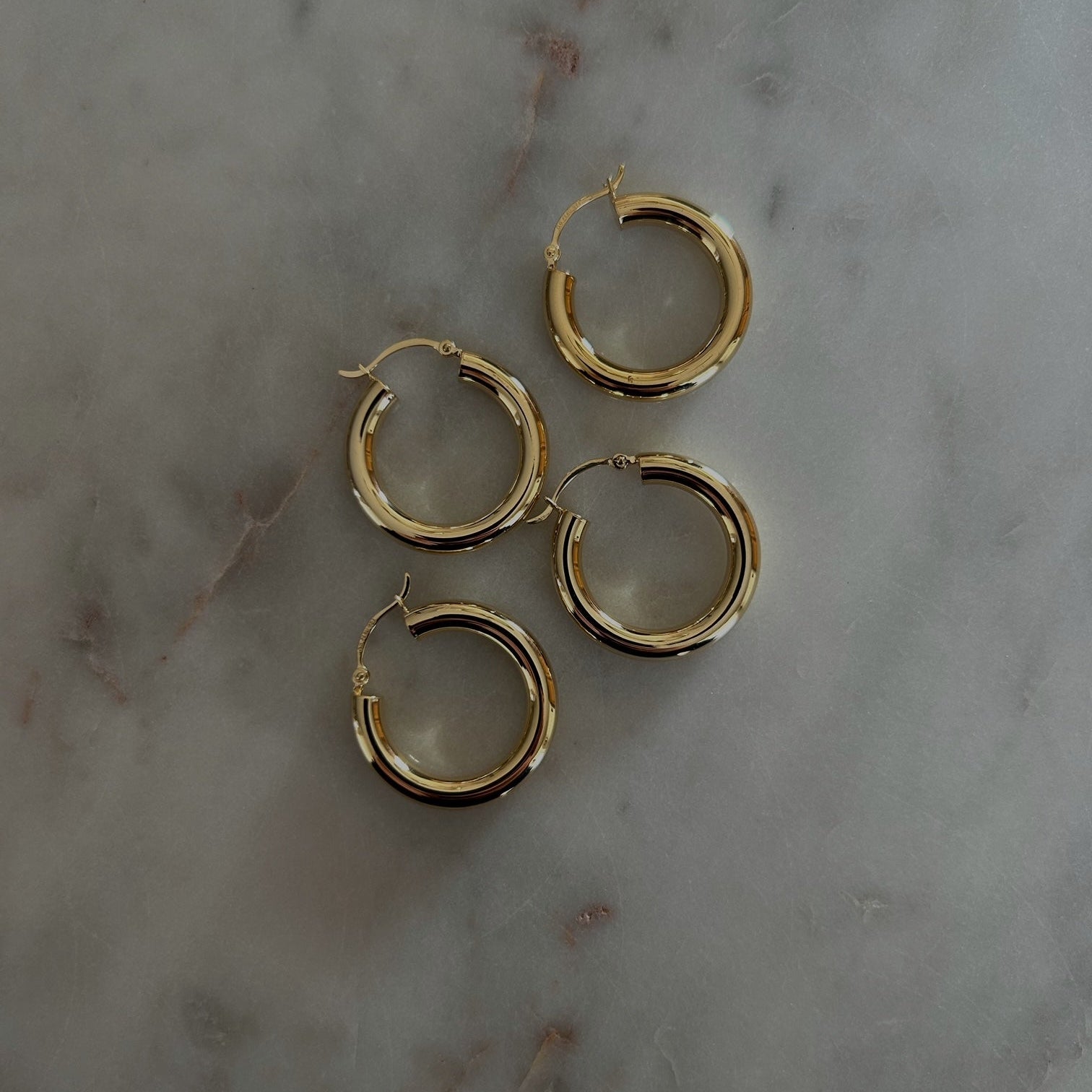 image of four gold hoops in a diagonal pattern on top of a marble table
