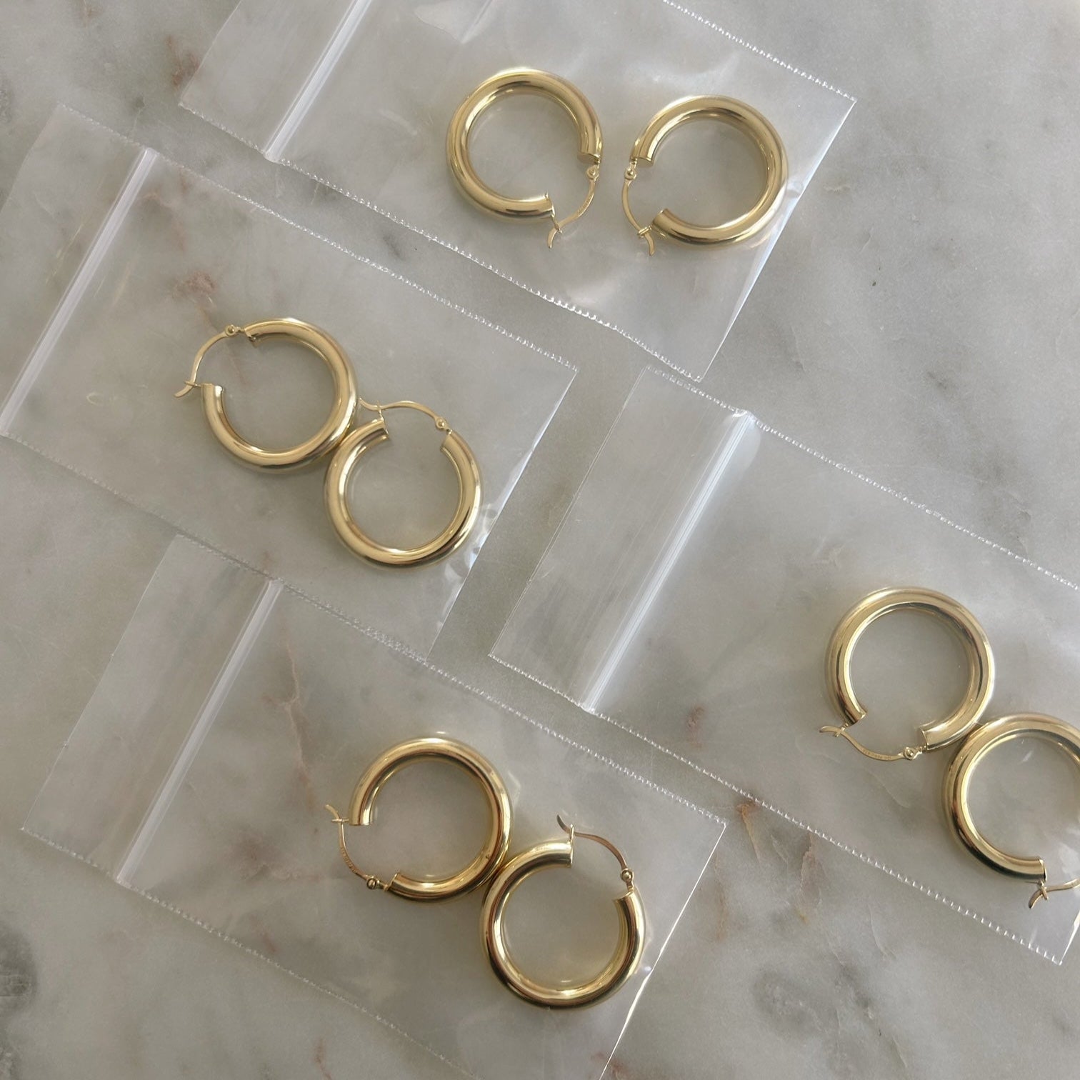 image of four pair of golden hoops in jewelry plastic bags on top of a marble table