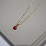 Gold necklace with a red pendant on a textured gray surface