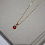 Gold necklace with a red pendant on a textured gray surface