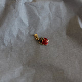 Small gold earring with a red gemstone on crumpled paper