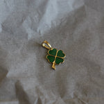 Gold pendant with green clover design on crumpled paper