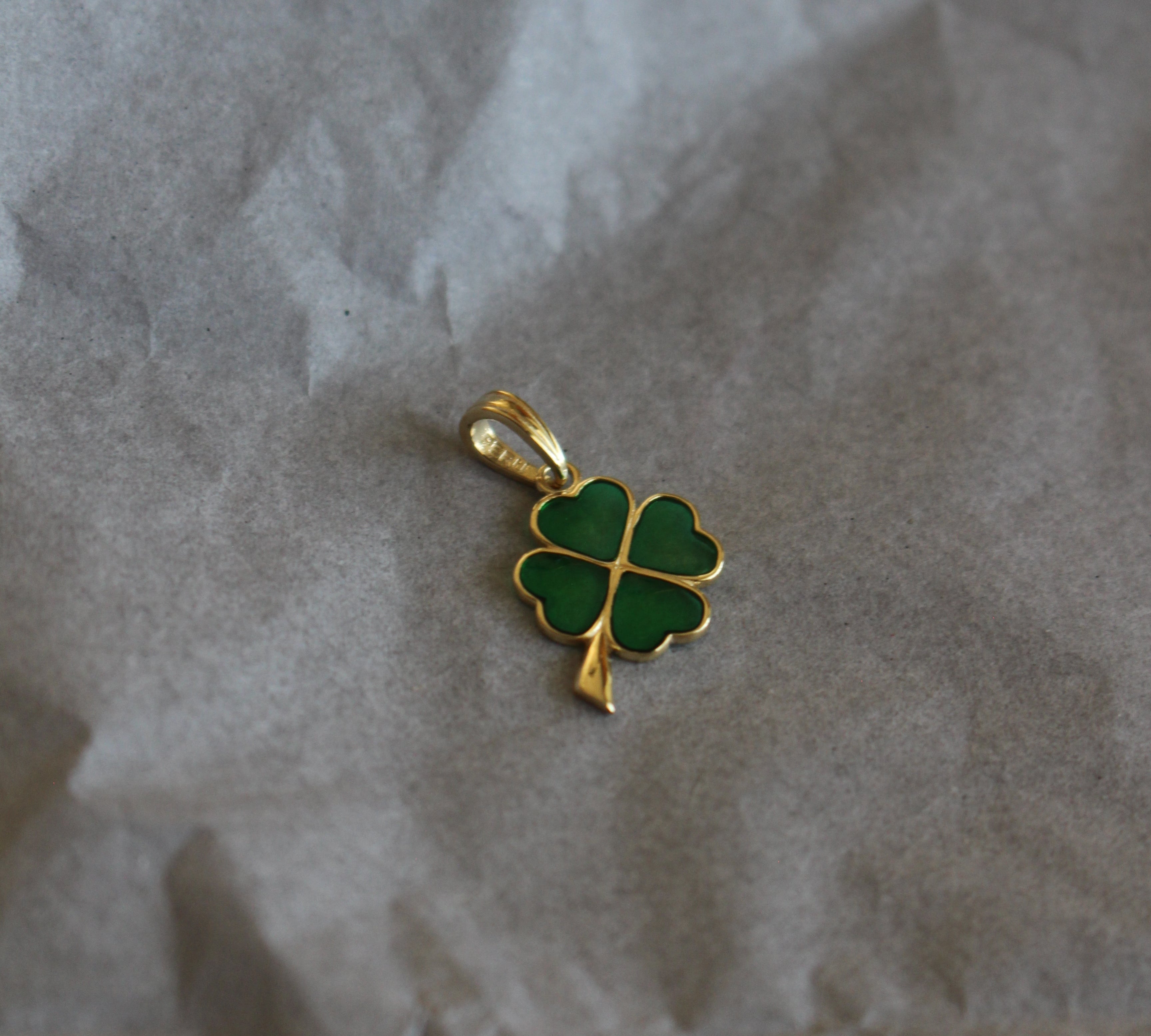 Gold pendant with green clover design on crumpled paper