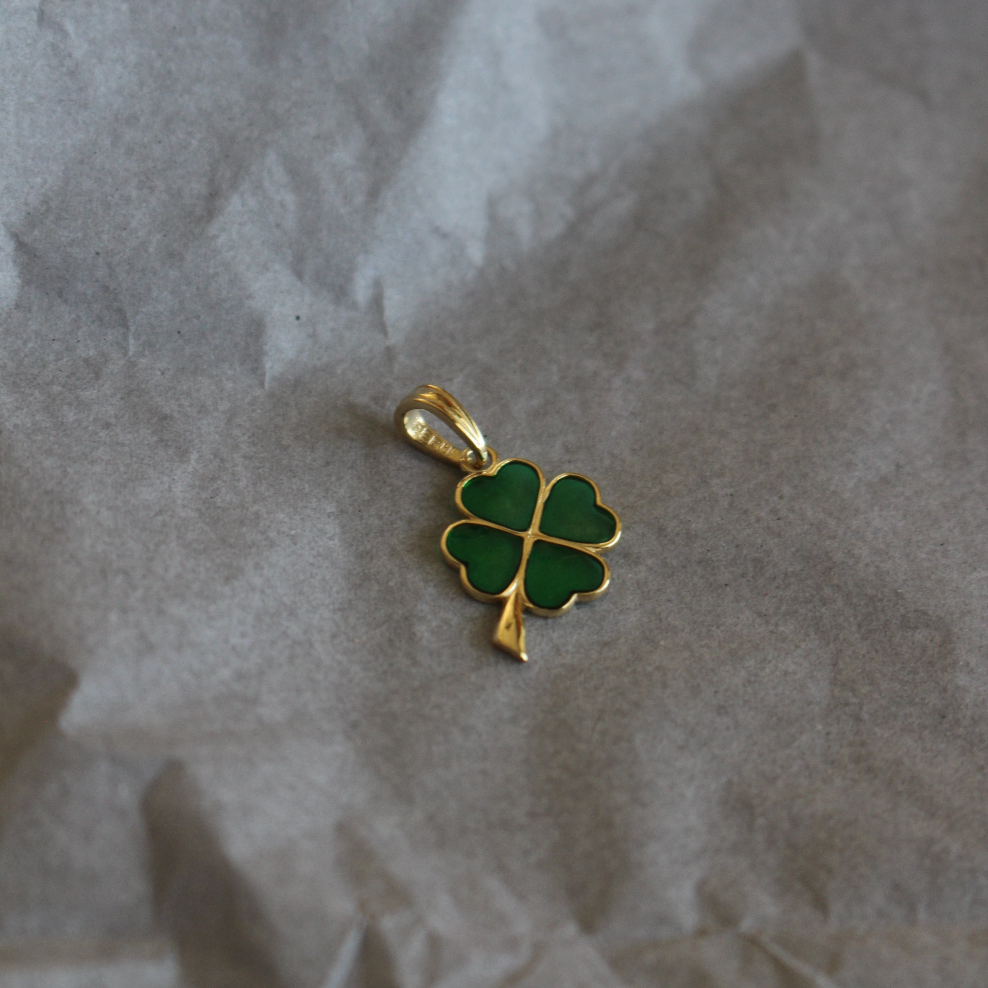 Gold pendant with green clover design on crumpled paper