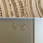 Top: Assorted gold chains on a beige background. Bottom: Two gold charms on a beige card.