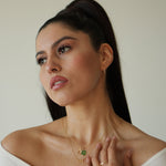 Woman wearing a necklace with a green pendant against a neutral background