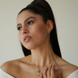 Woman wearing a necklace with a green pendant against a neutral background