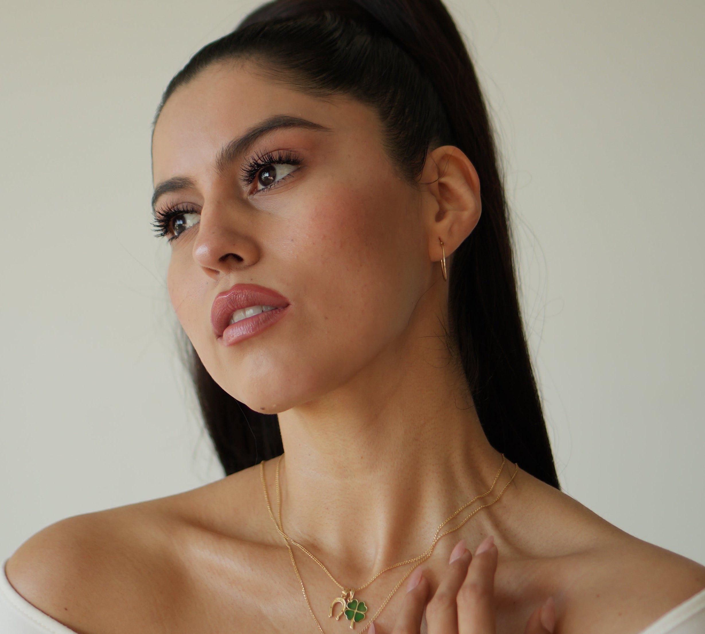 Woman wearing a necklace with a green pendant against a neutral background