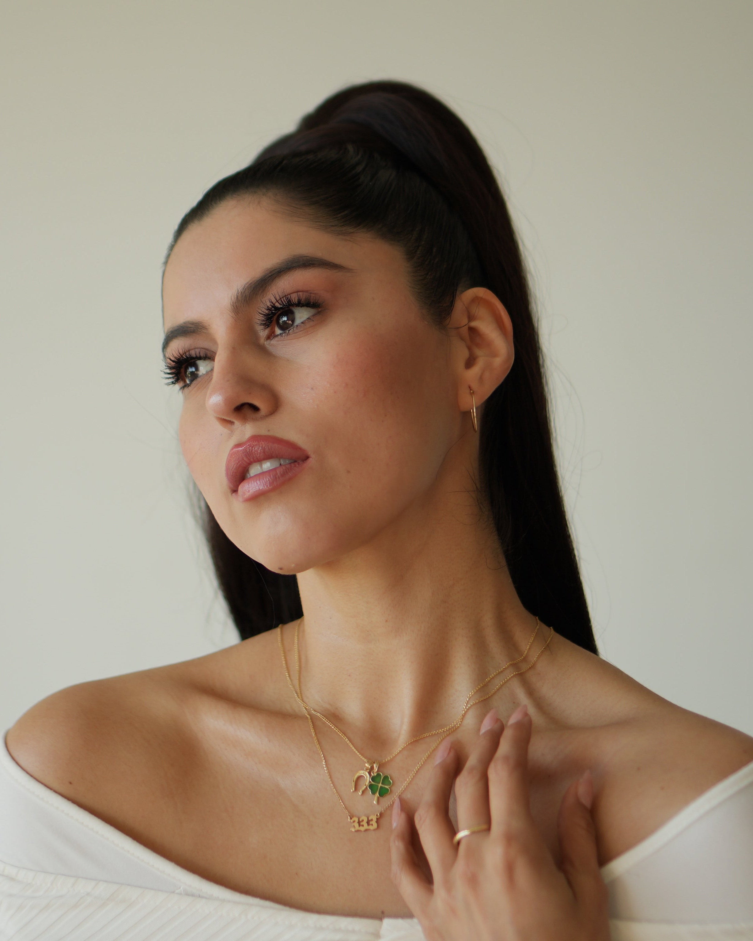 Woman wearing a necklace with a green pendant against a neutral background