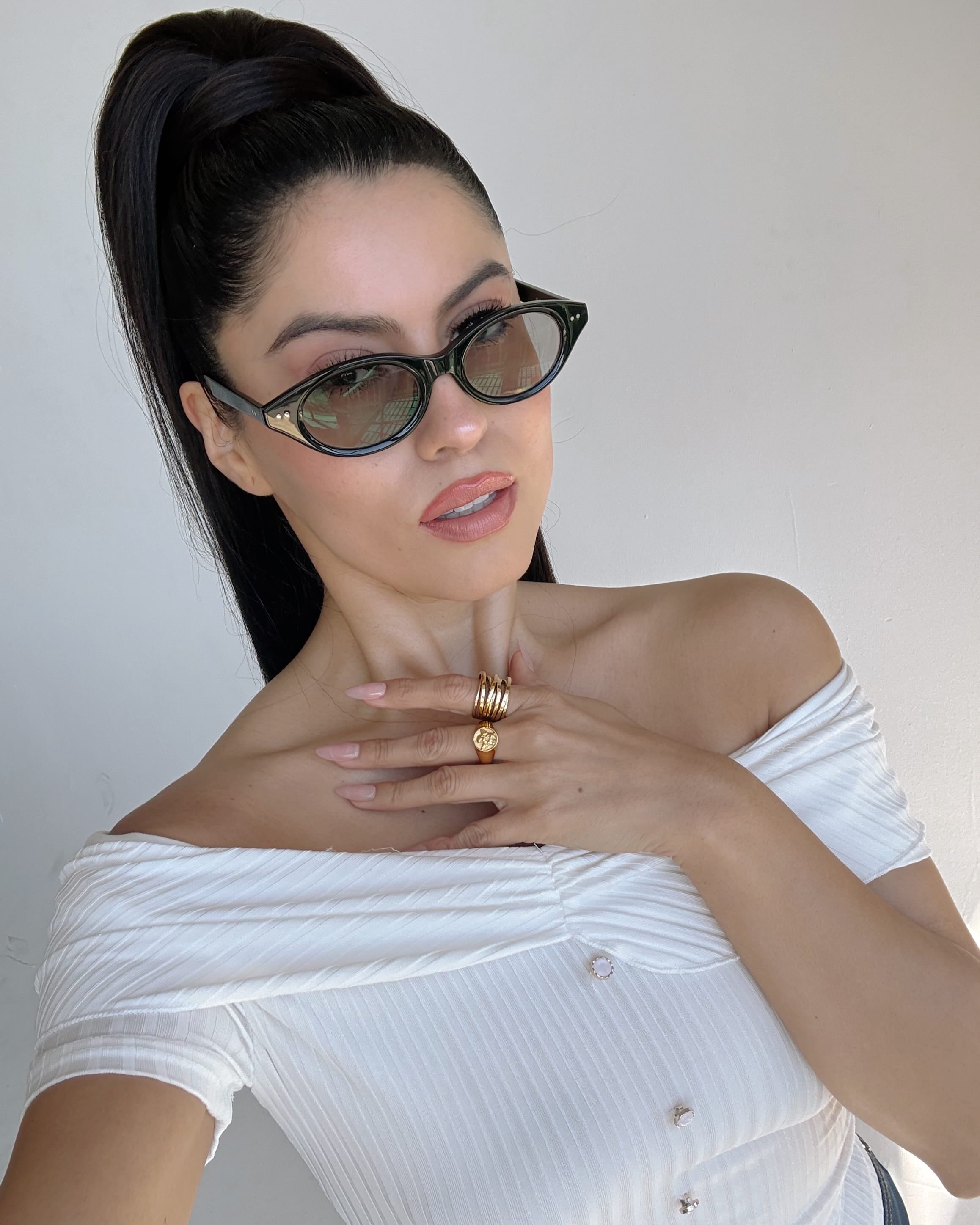 Woman wearing sunglasses and a white top with a plain background