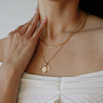 Person wearing a gold necklace with a pendant, touching their neck.
