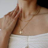 Person wearing a gold necklace with a pendant, touching their neck.