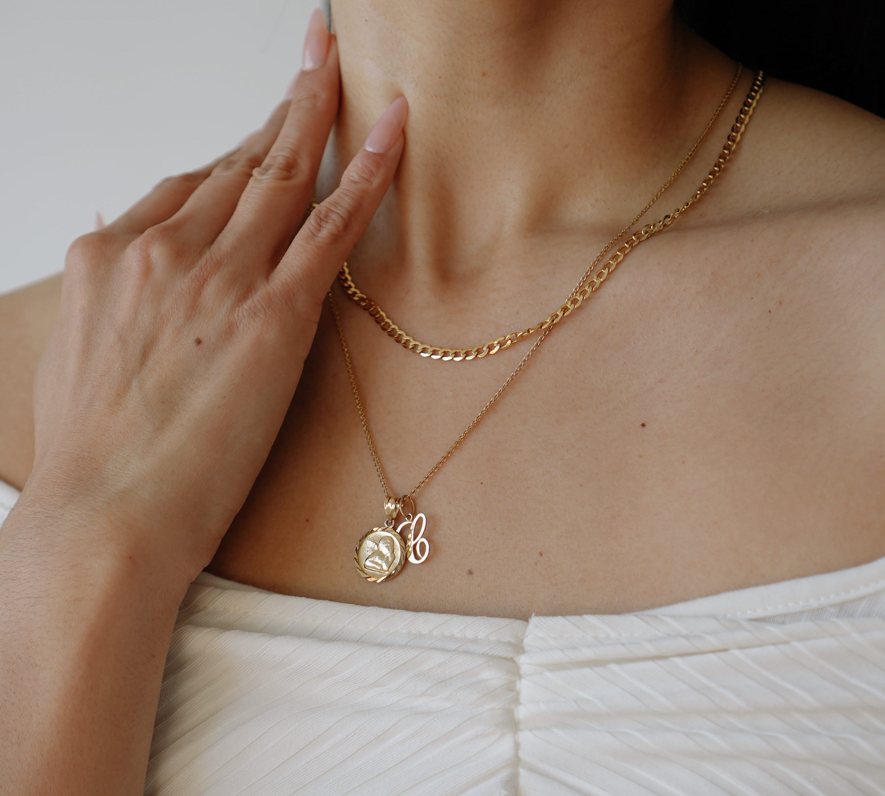 Person wearing a gold necklace with a pendant, touching their neck.