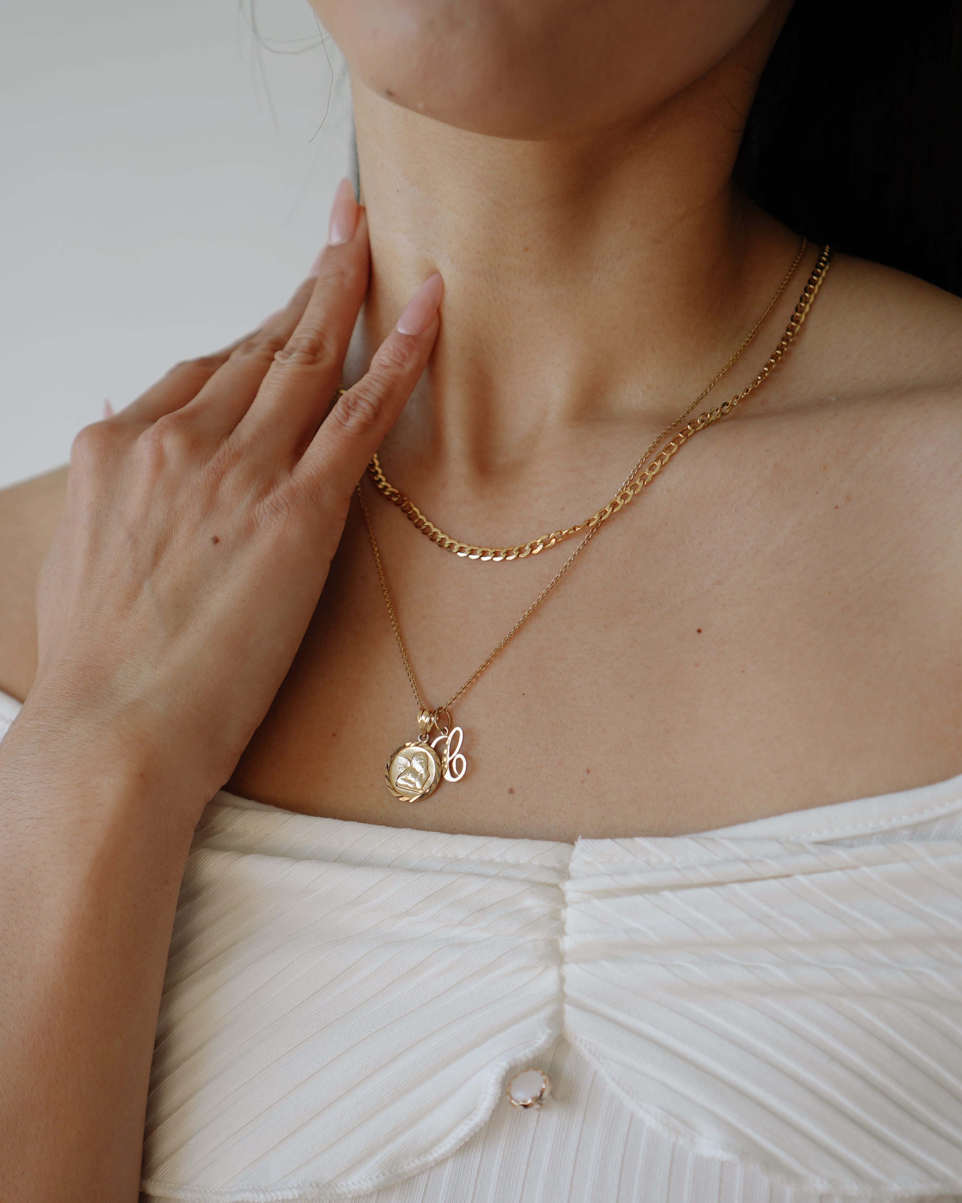 Person wearing a gold necklace with a pendant, touching their neck.
