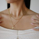 Close-up of a person wearing a gold necklace with a pendant.