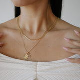 Close-up of a person wearing a gold necklace with a pendant.