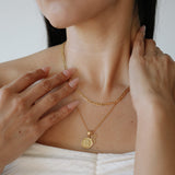 Close-up of a person wearing a gold necklace with a pendant, with hands adjusting the necklace.