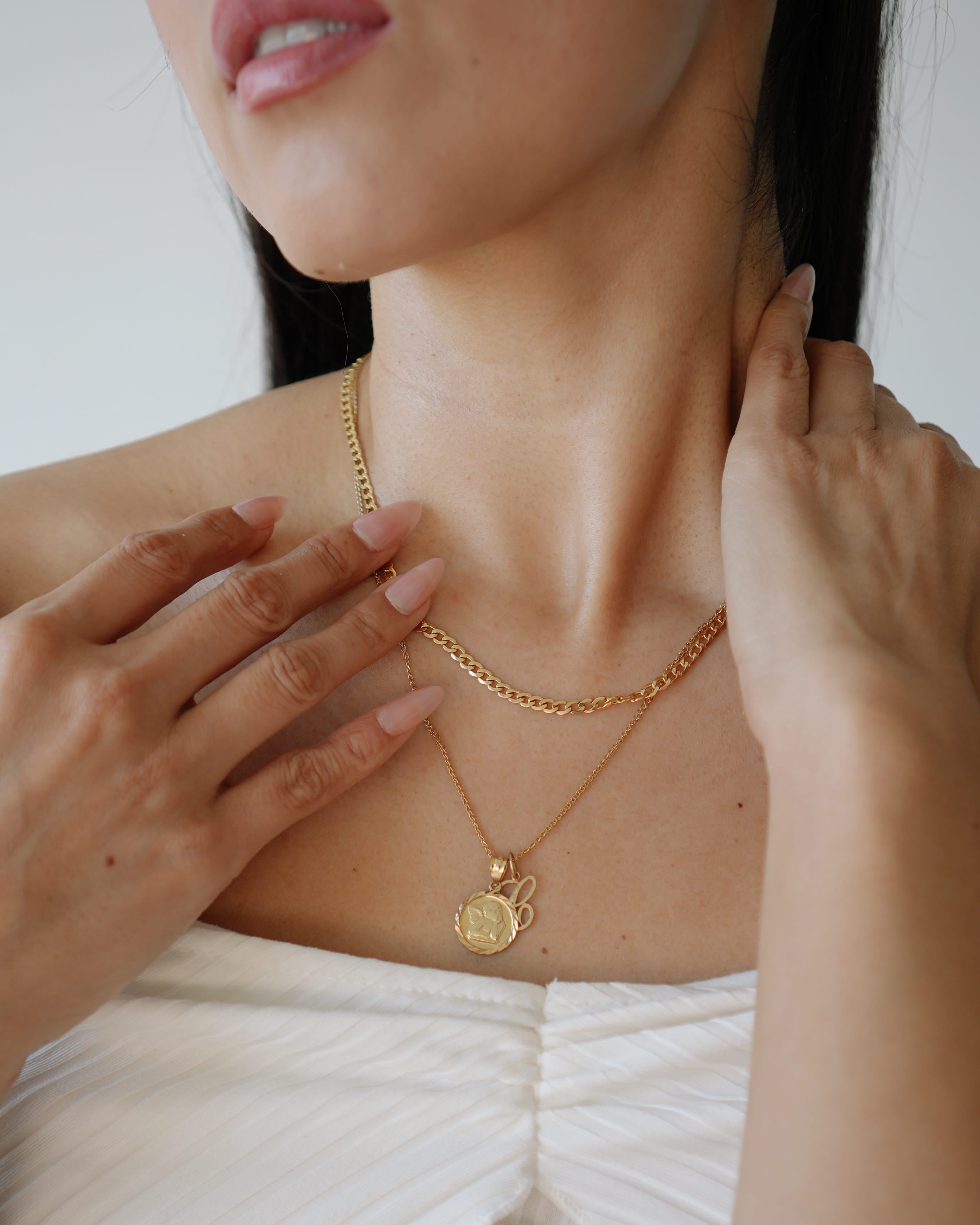 Close-up of a person wearing a gold necklace with a pendant, with hands adjusting the necklace.