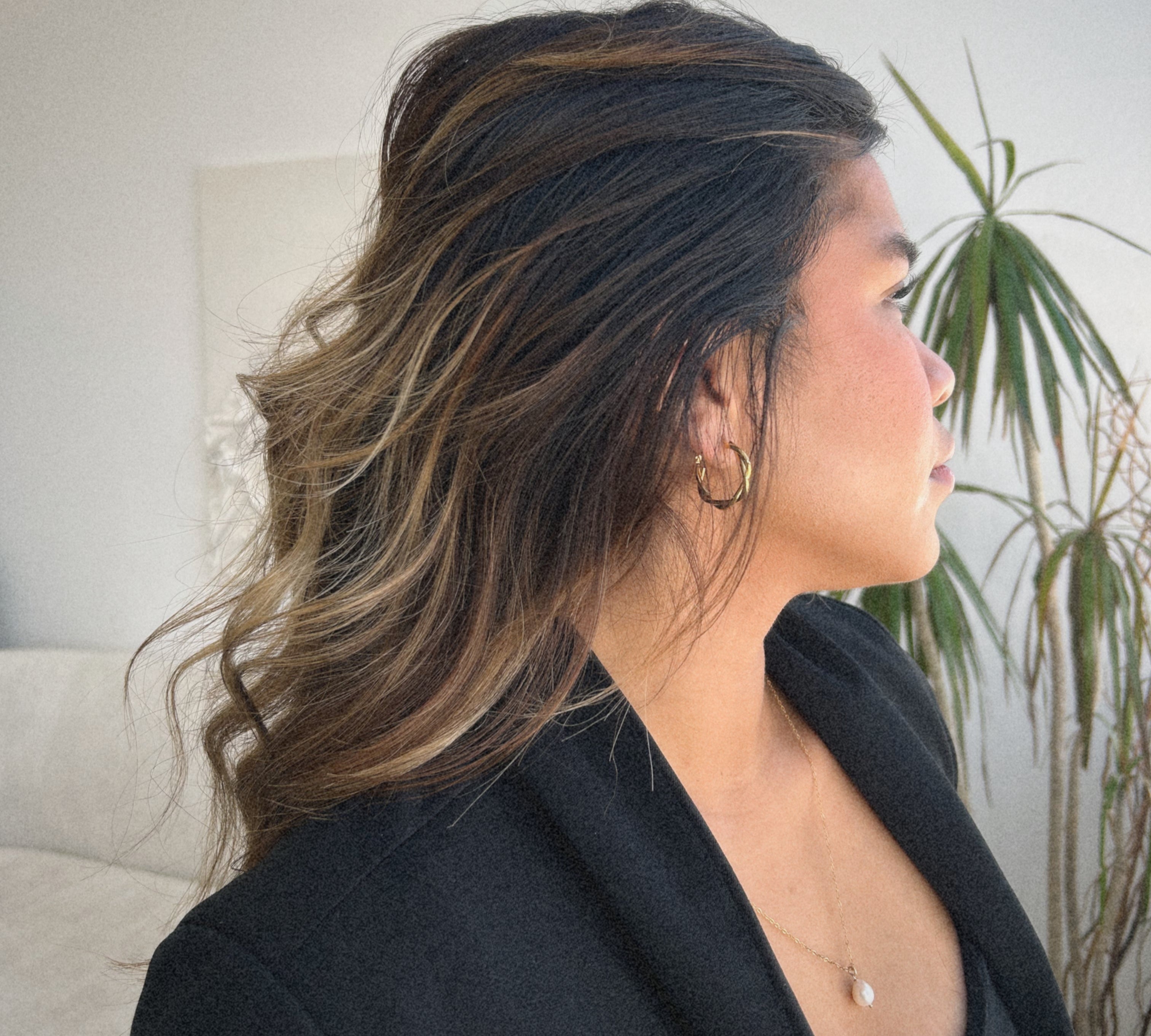 image of a woman looking off to the side wearing a gold twisted hoop and a pearl necklace
