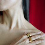 Close-up of a person wearing two gold rings on a blurred red background