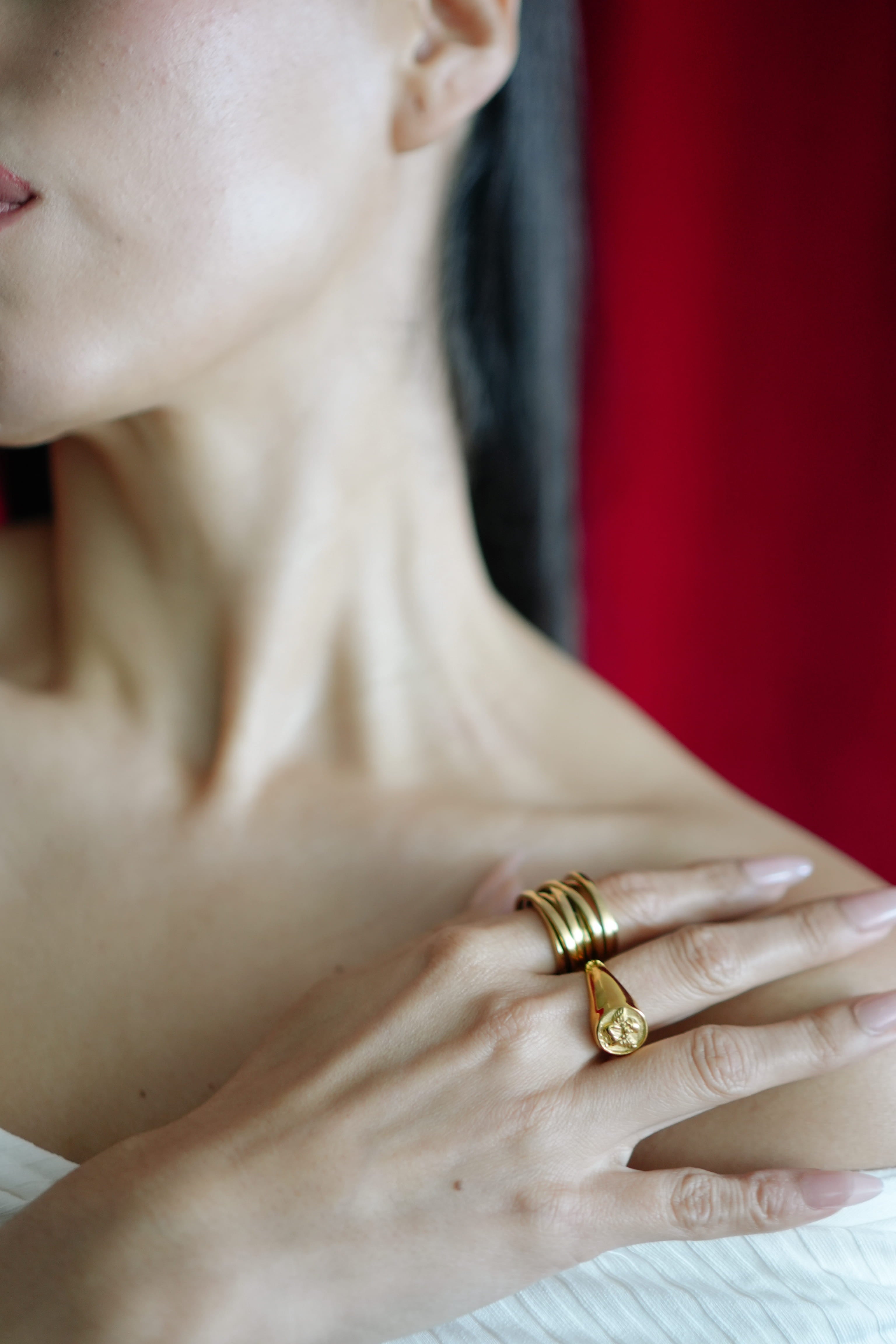 Close-up of a person wearing two gold rings on a blurred red background