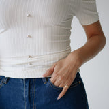 Person wearing a white ribbed top and blue jeans with a neutral background