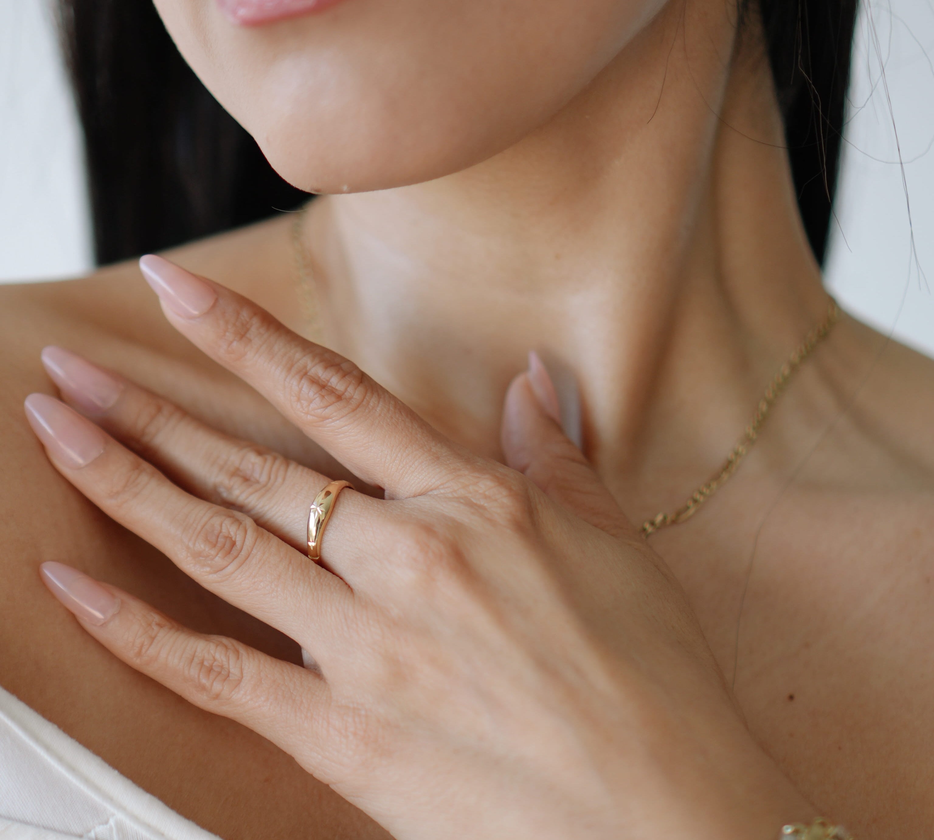 Close-up of a woman's hand wearing a gold ring and bracelet, with a blurred background.