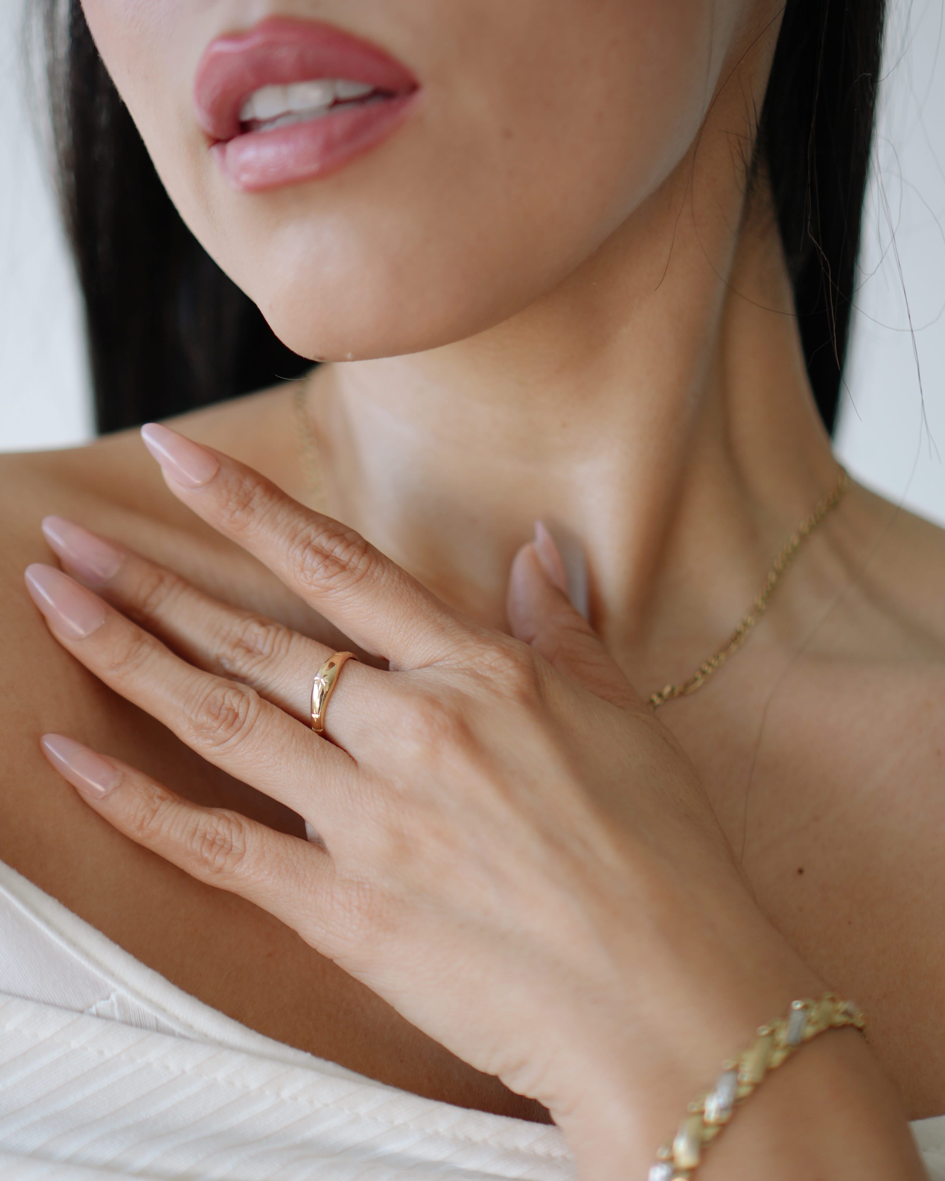 Close-up of a woman's hand wearing a gold ring and bracelet, with a blurred background.