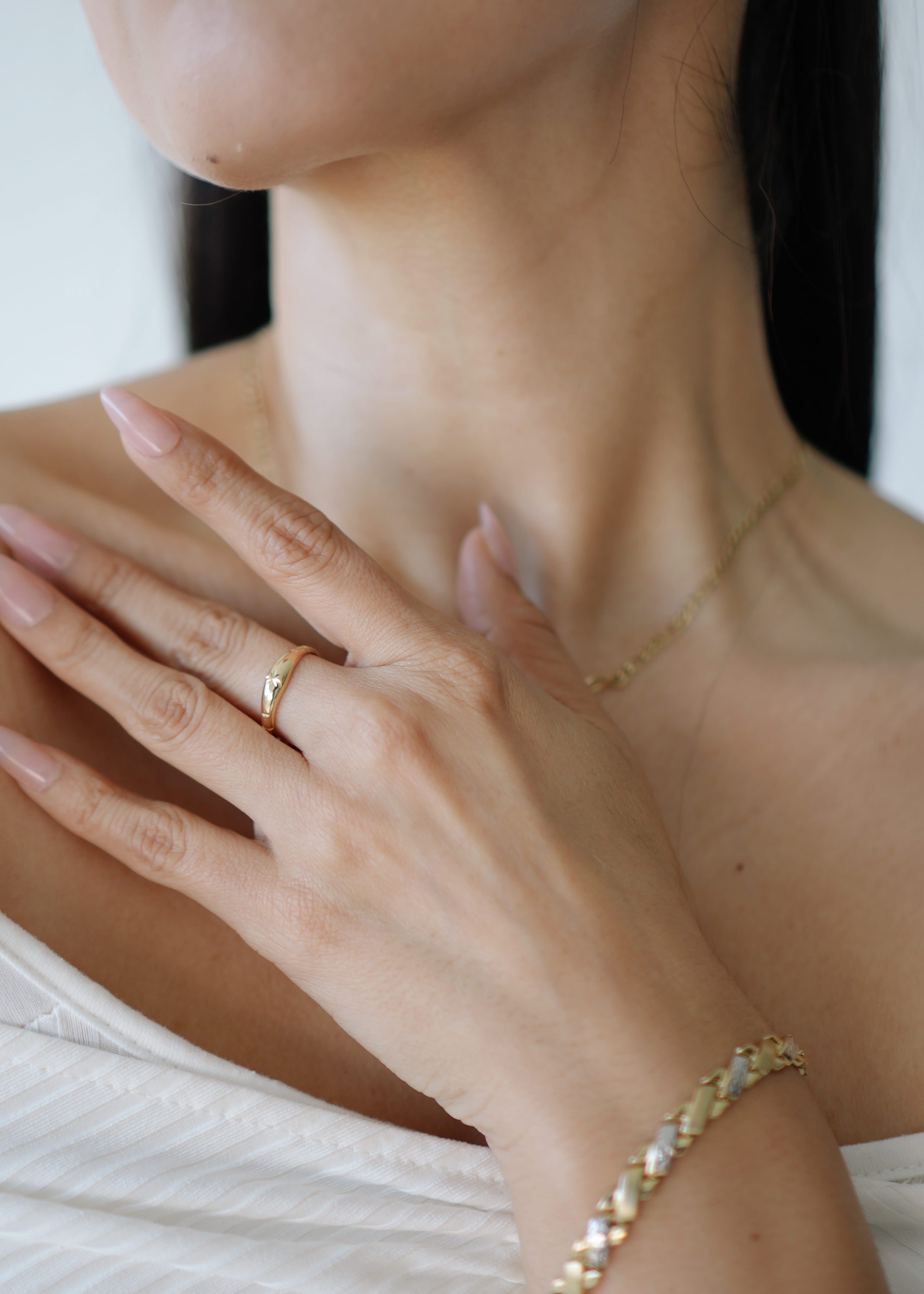 Close-up of a person wearing gold jewelry including a ring, necklace, and bracelet.