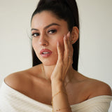 Woman in a white off-shoulder top with jewelry, against a plain background
