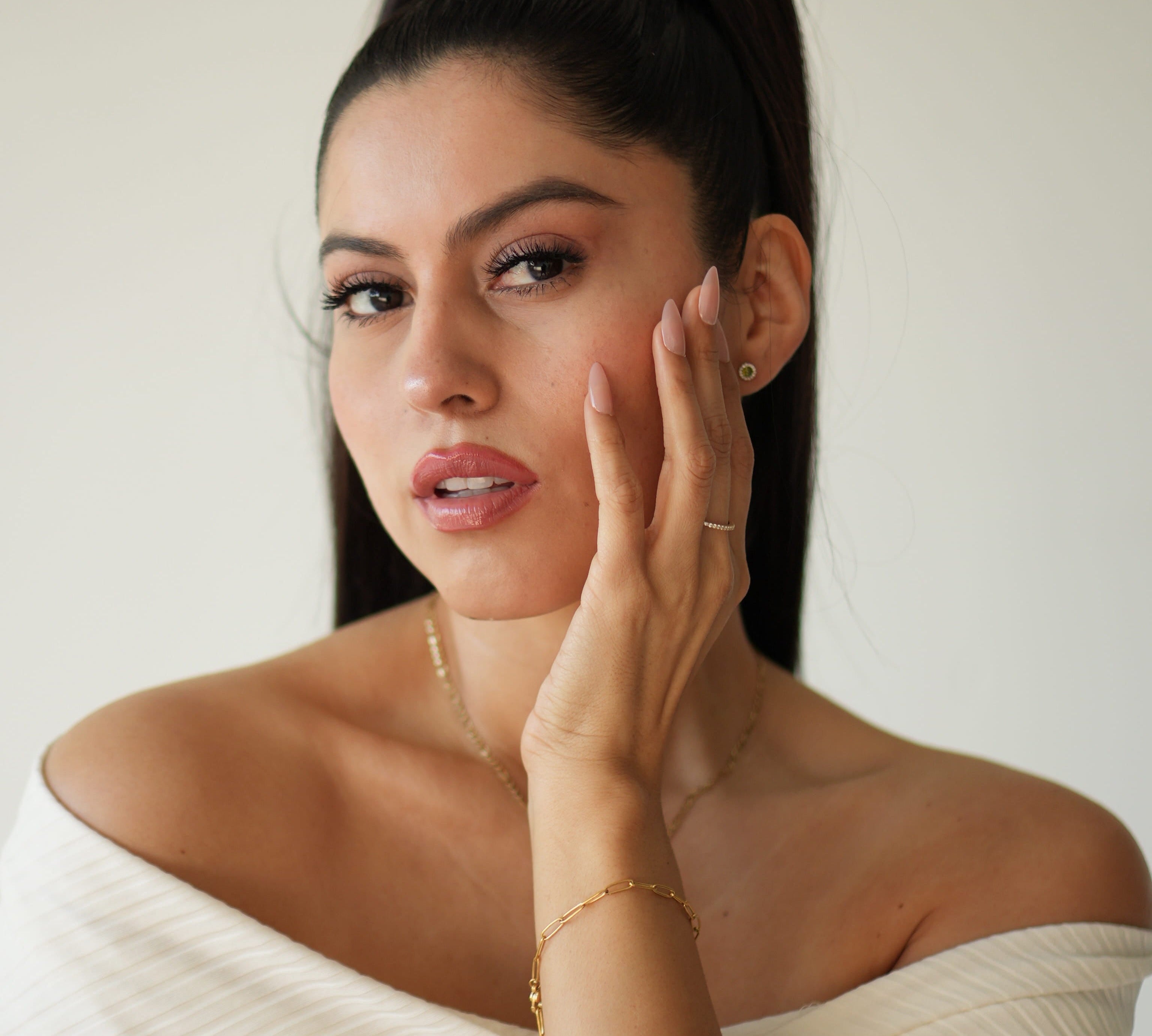 Woman in a white off-shoulder top with jewelry, against a plain background