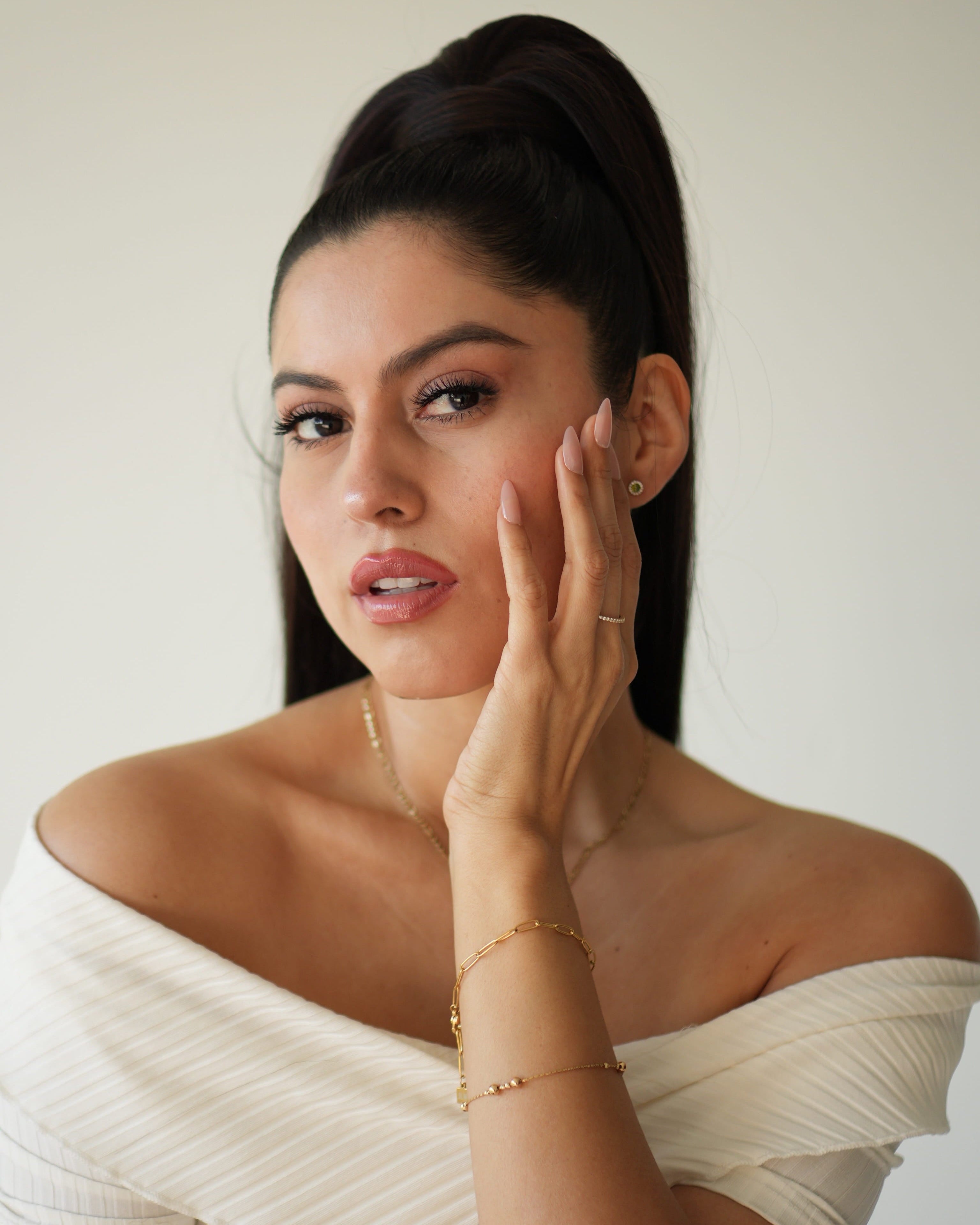 Woman in a white off-shoulder top with jewelry, against a plain background