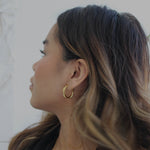 image of a woman wearing gold twisted hoops looking off to the side